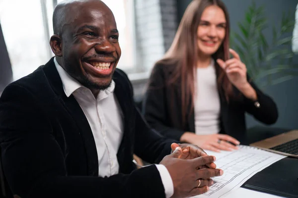 Szczęśliwy afrykański amerykański biznesmen i pracownik biurowy kobieta siedzi przy stole w biurze i śmieje — Zdjęcie stockowe