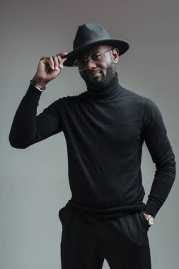 Şapkalı yakışıklı Afro-Amerikan adam eline dokunuyor ve cebinde gri bir arka plan var.