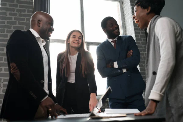 Grupo de empresários afro-americanos e mulheres trabalhadoras de escritório em ternos conversando umas com as outras enquanto estão perto da mesa — Fotografia de Stock