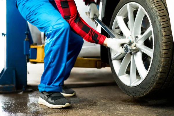 Muž mechanik drží klíč v rukou, zatímco stojí u volantu auta a mění pneumatiku — Stock fotografie