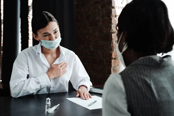 Азиатка-врач в халате и в медицинской маске просит сделать вакцину против вируса, подписывая бумаги пациенту — стоковое фото