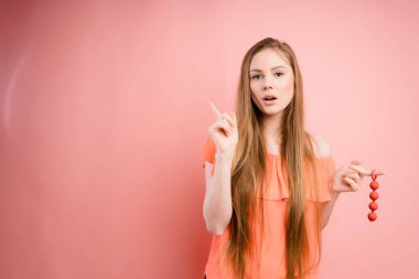 Woman with ginger hair holds dildo with open mouth and pointing her finger isolated on pink background. Sex toys 
