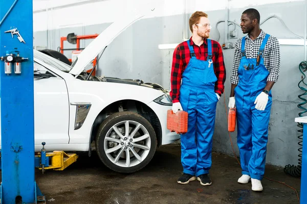 Afro-americký a bílý muž se zrzavými vlasy, stojící s přístroji u rozbitého bílého auta. Připraveno k opravě — Stock fotografie