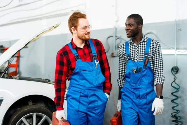 Afro Američan a muž s rudými vlasy jsou dikusment proces opravy auta za nimi. Mechanika pracuje — Stock fotografie