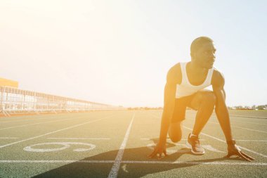 Siyah şortlu bir Afro-Amerikalı stadyumda güneşin arka planına doğru koşmaya başlıyor.