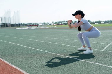 Gri takım elbiseli Taylandlı bir kız stadyuma çömelmiş ve kasten bakıyor.