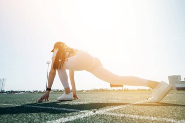 Şapkalı beyaz tenli bir kız stadyumda yarışa hazırlanıyor.