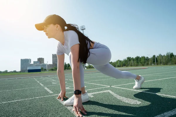 Una chica de piel blanca con gorra se prepara para una carrera en el estadio — Foto de Stock