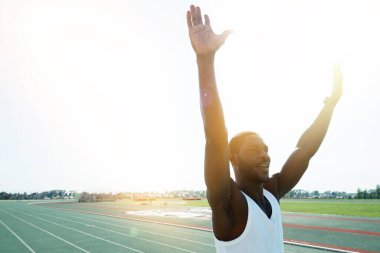 Koyu tenli bir erkek atlet spor üniformalı bir sporcu bitiş çizgisine ilk geldiği ve ellerini kaldırdığı için mutlu.