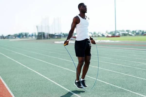 Un atleta de pista y campo afroamericano con una camiseta blanca entrena antes de una carrera de cuerda de salto Imagen De Stock