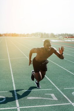 Erkek bir Afro-Amerikan atlet çıplak bir gövdeyle stadyumda uzun bir mesafe koşuyor.