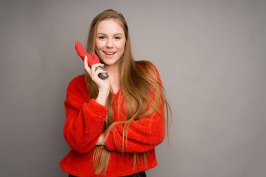 A beautiful Italian girl in a red sweater happily holds a vibrator or a dildo in her hands for sex
