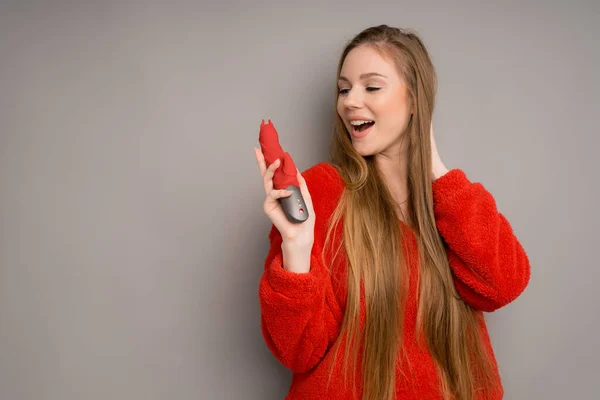 Ein attraktives Mädchen europäischen Aussehens in rotem Pullover hält glücklich einen roten Phallus in der Hand Stockbild