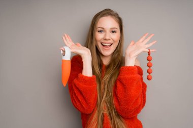 Kafkas görünümlü güzel bir kız ellerinde seks oyuncakları tutuyor ve gri bir arka planda gülümsüyor. Seks için masaj aleti ve kadınlar için orgazm olmak için vibratör..