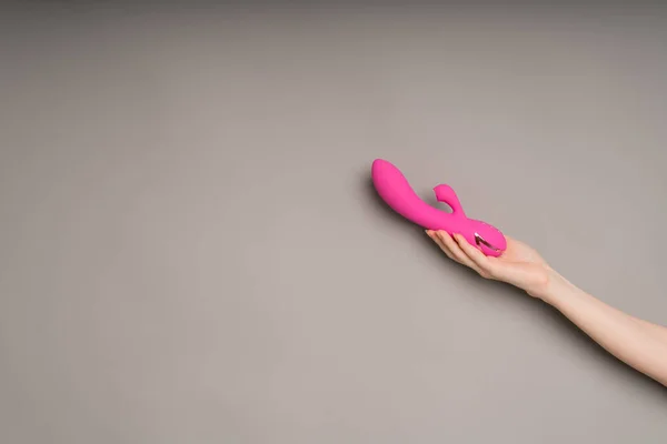 Bright pink vibrator in a female hand on an orange background. Massager for masturbation. Dildo, toys for adults — стоковое фото