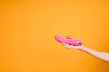 Sex gadgets and masturbation devices. Pink dildo in womans hand on orange background. sex toys