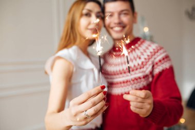 Genç evli çift ellerinde maytap tutuyor. Noel ağacının yanında dur, Noel 'de