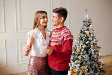 Genç evli çift ellerinde maytap tutuyor. Noel ağacının yanında dur, Noel 'de