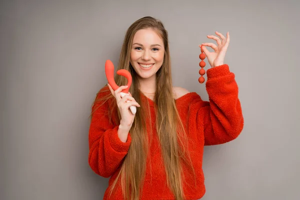 An attractive girl in a sweater depicts the emotion of happiness, smiling.holding a red dildo, vaginal balls in her hand 图库照片