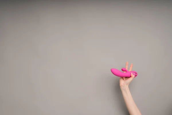 O mână feminină deține un vibrator roz sau un vibrator pentru sex.Pe un fundal gri. Util pentru un magazin de sex — Fotografie, imagine de stoc