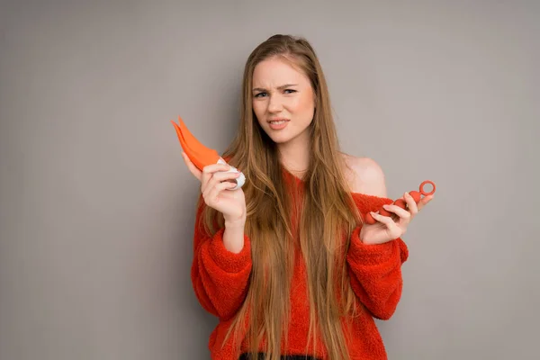 An attractive girl in a sweater depicts an emotion of disgust, smiling.holding a red dildo, vaginal balls in her hand — Stock fotografie