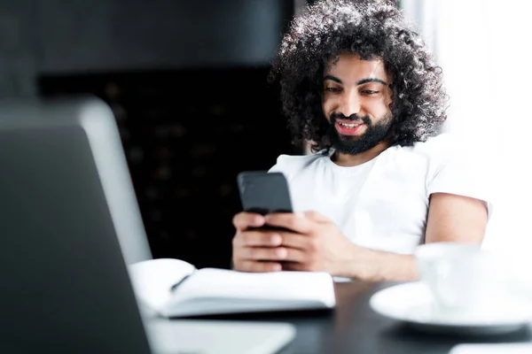 Een Afro-Amerikaanse man glimlacht breed en zit aan de telefoon voor het begin van de conferentie op een laptop Stockfoto