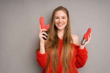 Kafkas görünümlü bir kız gülümseyerek gri bir arka planda seks için iki vibratör ya da vibratör tutuyor.