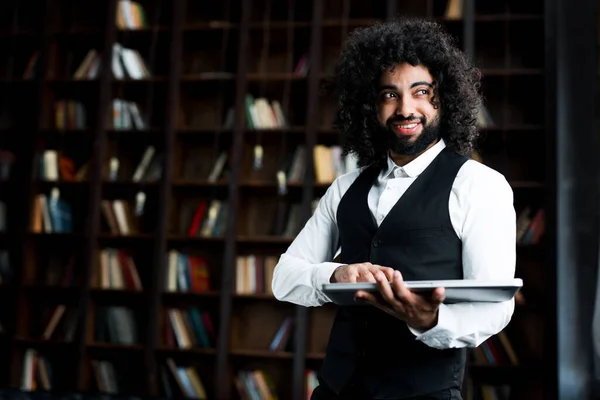 Счастливый красивый египетский студент готовится к лекции в библиотеке, держа в руках книгу — стоковое фото