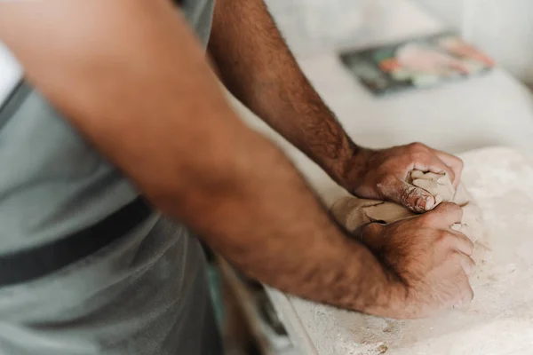 Argila de ceramică este agitată și sfărâmată de mâini de un bărbat pe o masă într-un studio de hobby Fotografie de stoc