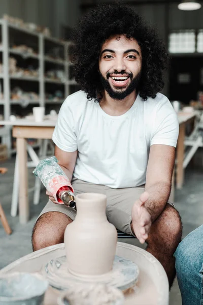 Afro-vlasý hrnčíř vytesává keramický hrnec z hlíny na hrnčířském kole. Workshop, umělecký koncept — Stock fotografie