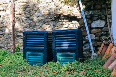 Bahçede iki plastik gübre kutusu ve arka planda taş duvar.