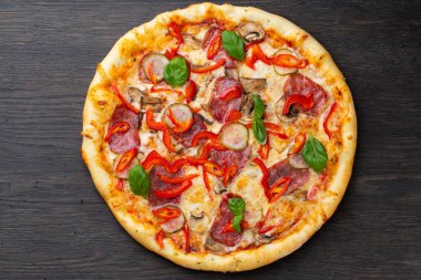 Eritilmiş mozarella peynirli İtalyan pizzası, zeytin ve sosis taze sebze ve fesleğen yapraklarıyla süslenmiş.