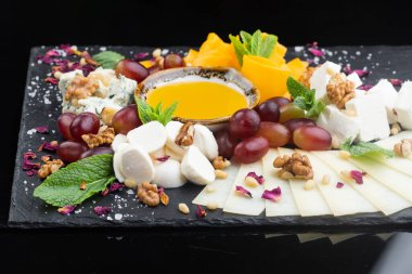 Bal, fındık ve üzümlü peynir tabağı siyah bir taş tahtada.