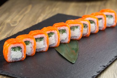 Siyah zemin üzerinde kırmızı havyar, somon, ton balığı, salatalık ve avokado ile uramaki suşi ruloları yakın çekim. Suşili lezzetli geleneksel Japon yemekleri..