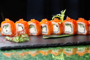 Somon, füme yılan balığı, avokado ve siyah arka planda krem peynirli suşi rulosu (Philadelphia). Suşi menüsü. Japon yemeği..