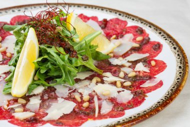 Carpaccio bifteği, parmesanlı soğuk aperatif, kapari ve roka beyaz tabakta..