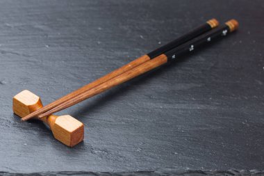 Beyaz arka planda siyah tahta. Beyaz desenli arka planda boş siyah granit taş dikdörtgen tahta. Taştan bir tahtadaki bardak altlıklarında suşi için çubuklar.