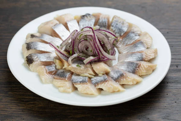 pieces of salted fish with pickled onions. Scandinavian herring appetizer on a white plate