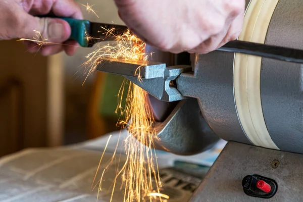 Close-up: the hands of a master sharpen a knife on a sharpening machine. Selective focus. Lots of bright glowing sparks.