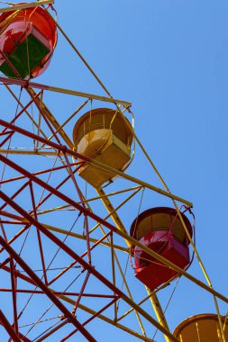 Bir yaz günü lunaparktaki dönme dolabın çok renkli kabinlerinin alt görüntüsü. Mavi gökyüzüne karşı sarı ve kırmızı kulübeler. Dikey çekim