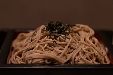 Japon usulü soğuk erişte, kahverengi arka planda küçük bir kasede sos çorbası.