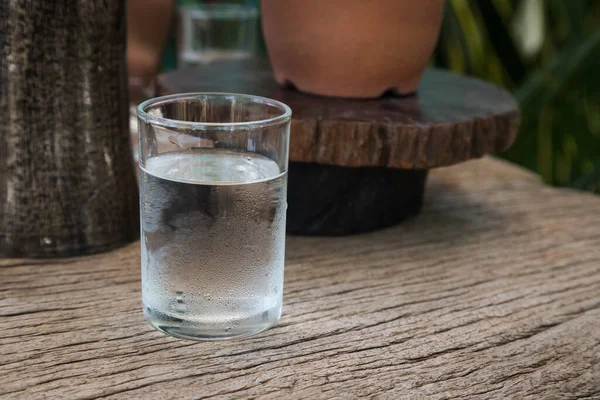 cold water in cup put on bark wooden table with some natural decoration on background