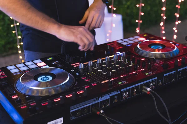 DJ is mixing some music with controller at outdoor night party, by moving hand so fast to set many button