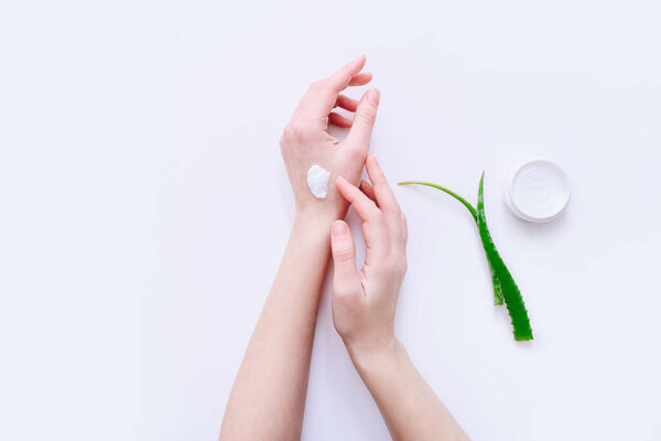 Woman applying organic cream on hands, aloe vera leaves and cream container on white surface