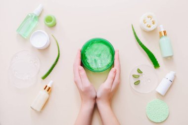 Kadın elleri aloe jeli tutuyor. Aloe Vera yaprakları ve bej yüzeyde kozmetik ürünler. Üst görünüm