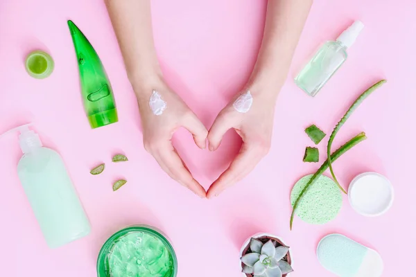 Manos de mujer con crema en forma de corazón. Productos cosméticos naturales sobre fondo rosa, vista superior — Foto de Stock