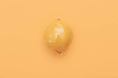 Turuncu arka planda polietilen plastiğe sarılı bir limon. Asgari çevresel konsept. Düz düz, üst görünüm