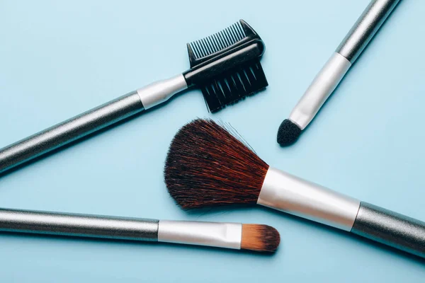 Set of makeup brushes scattered on blue background. Top view point, flat lay. — Stok fotoğraf