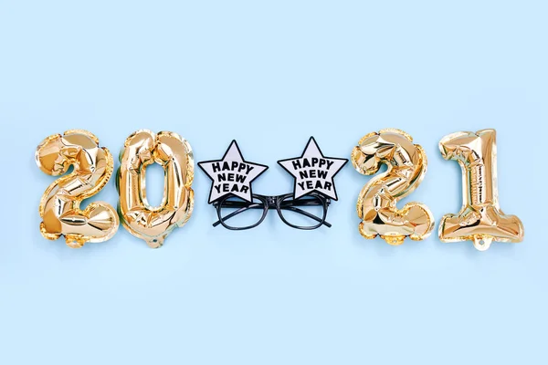 Balony foliowe w postaci cyfr 2021 i świąteczne okulary na niebieskim tle. Dekoracje noworoczne. Widok z góry — Zdjęcie stockowe