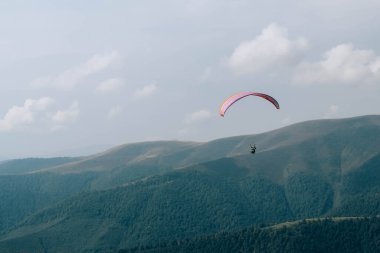 Paraglide silueti Carpathian tepeleri ve bulutları üzerinde uçuyor.